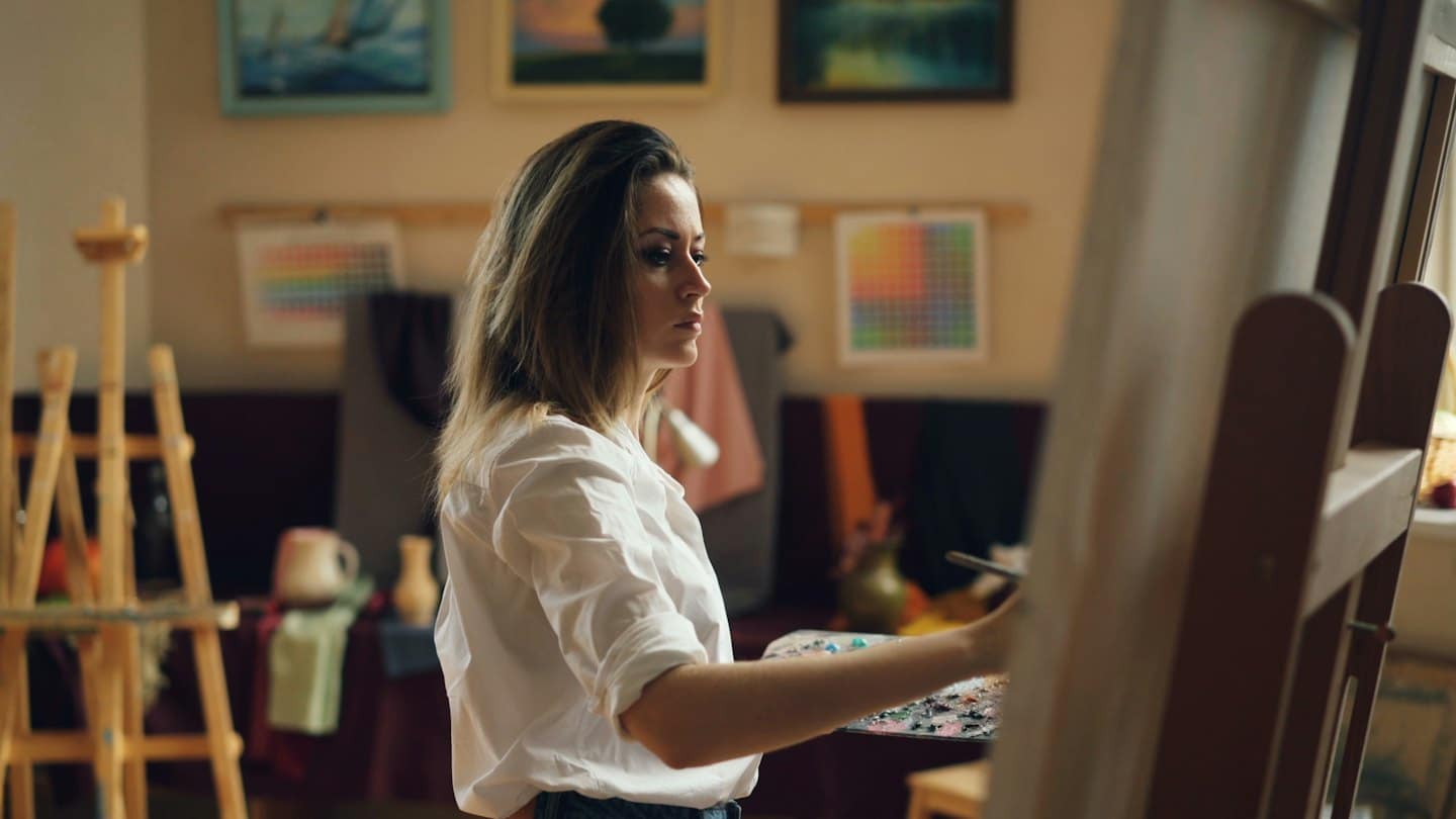 Artista in camicia bianca dipinge su tela in studio.